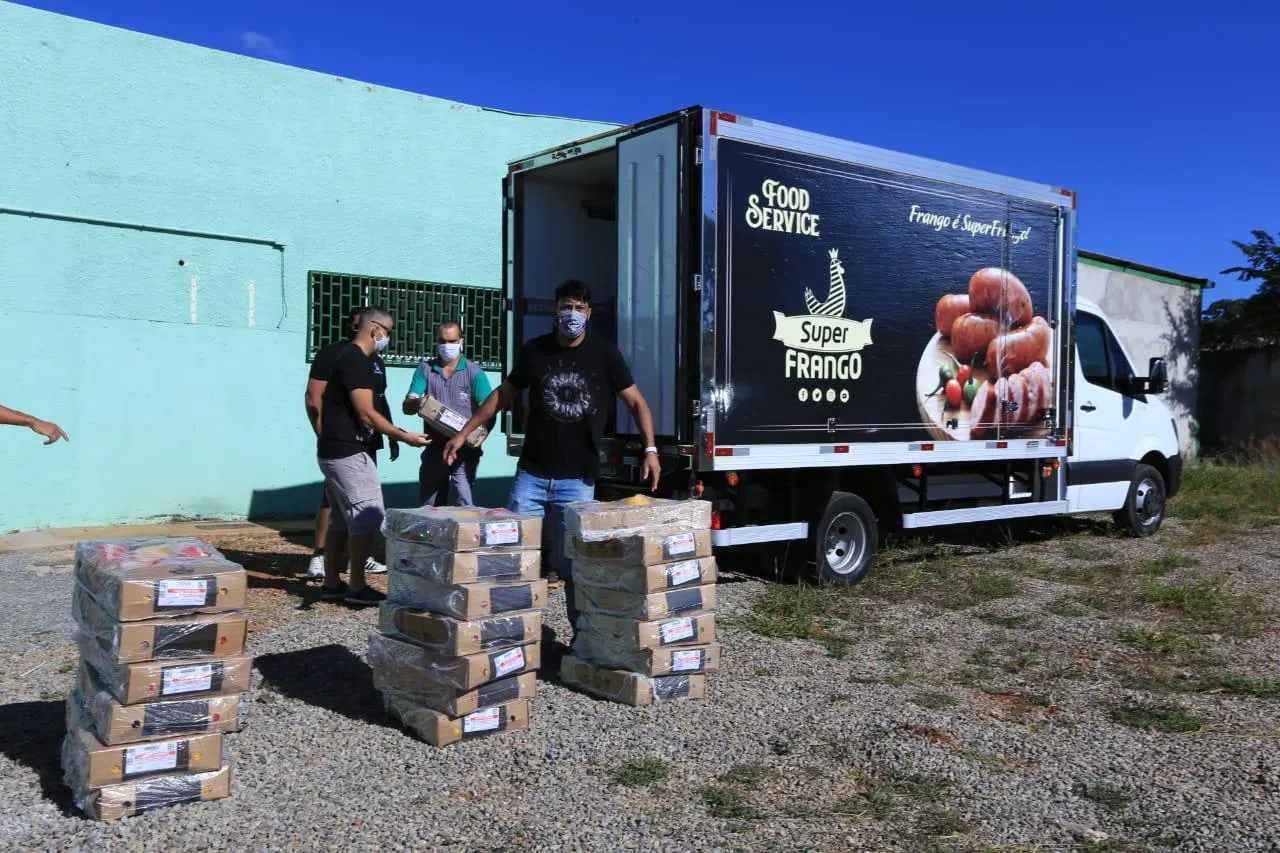 Caminhão de entregas ao lado de pilhas de caixas de alimentos, com homens de máscara descarregando.