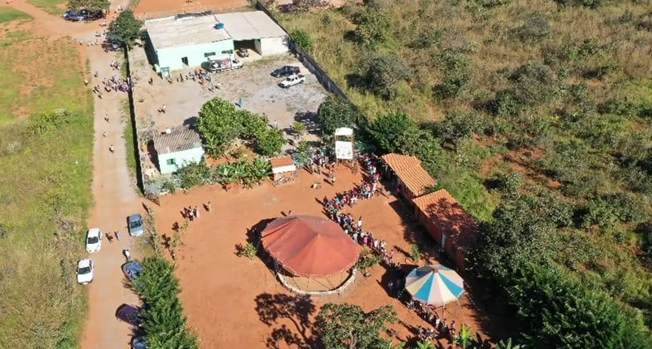 Vista aérea de um terreno de terra vermelha com construções e uma cobertura redonda, cercado de vegetação do Cerrado.