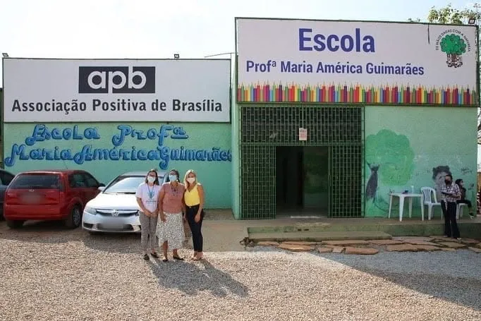 Fachada da Escola Professora Maria América Guimarães e da Associação Positiva de Brasília, com três mulheres de máscara à frente.