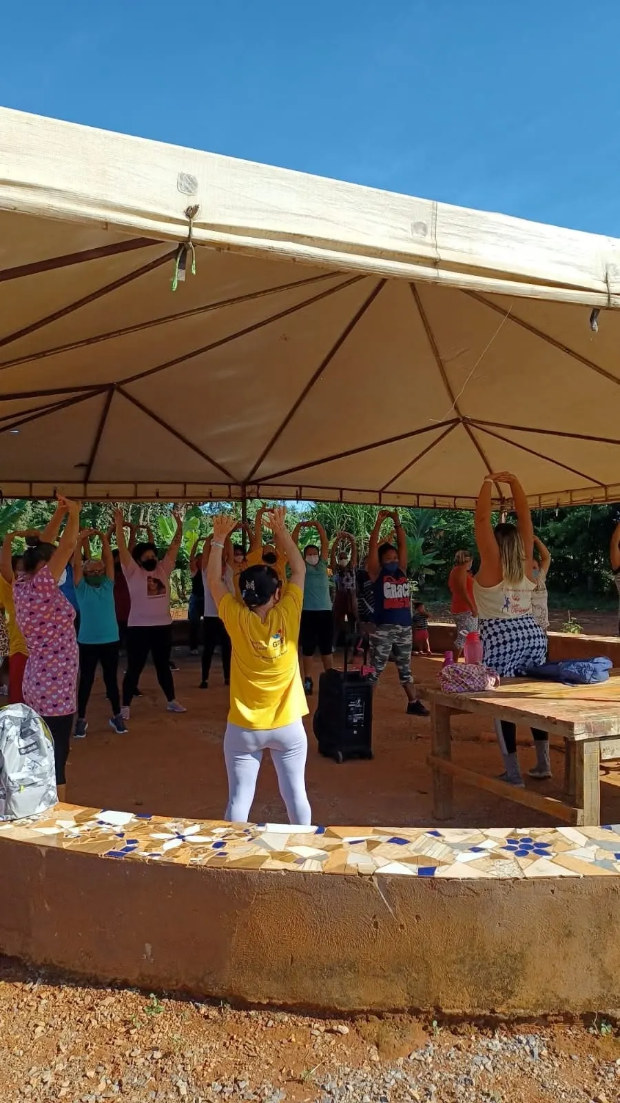 Mulheres vistas de costas erguem os braços em uma aula de zumba sob uma grande tenda.