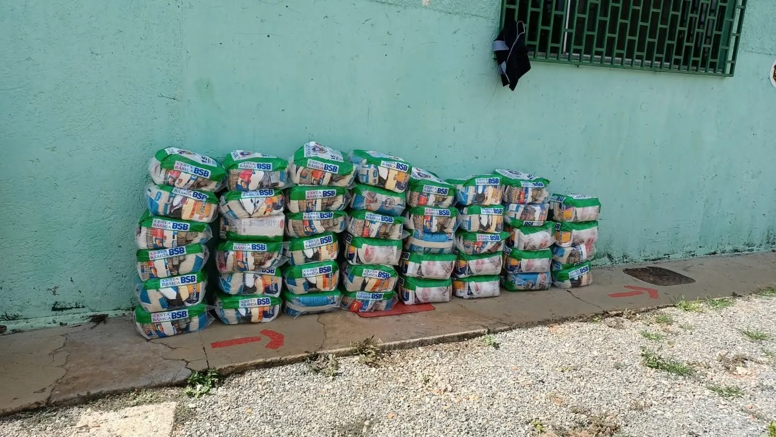 Cestas básicas empilhadas junto a uma parede verde, prontas para a entrega.