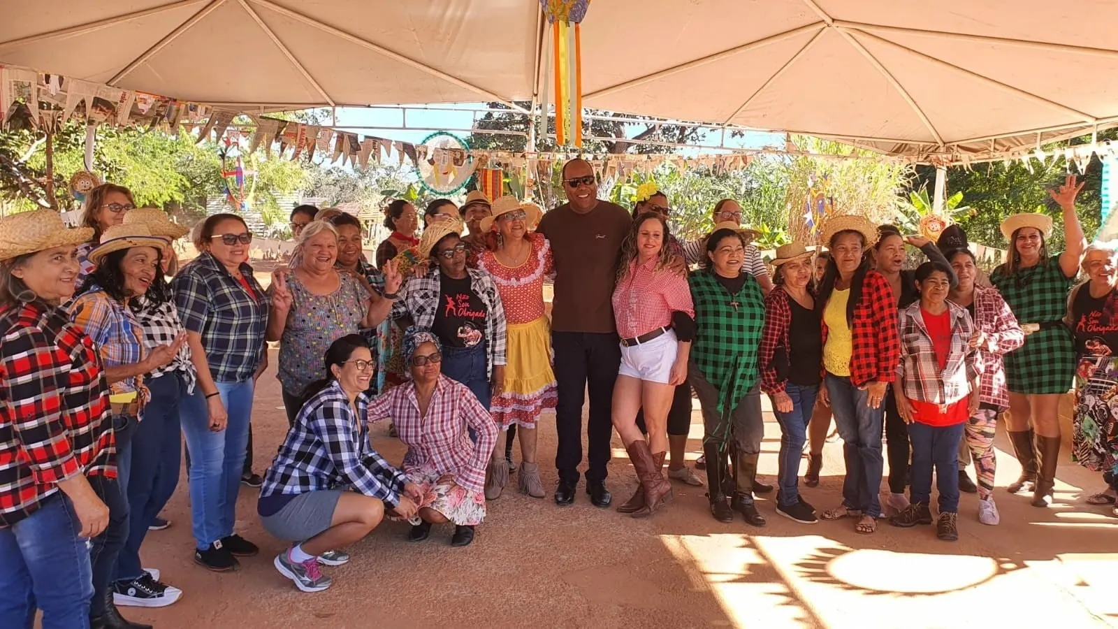 Grupo de idosos e convidados em trajes de festa junina posando sob uma tenda no Espaço Quilombo.