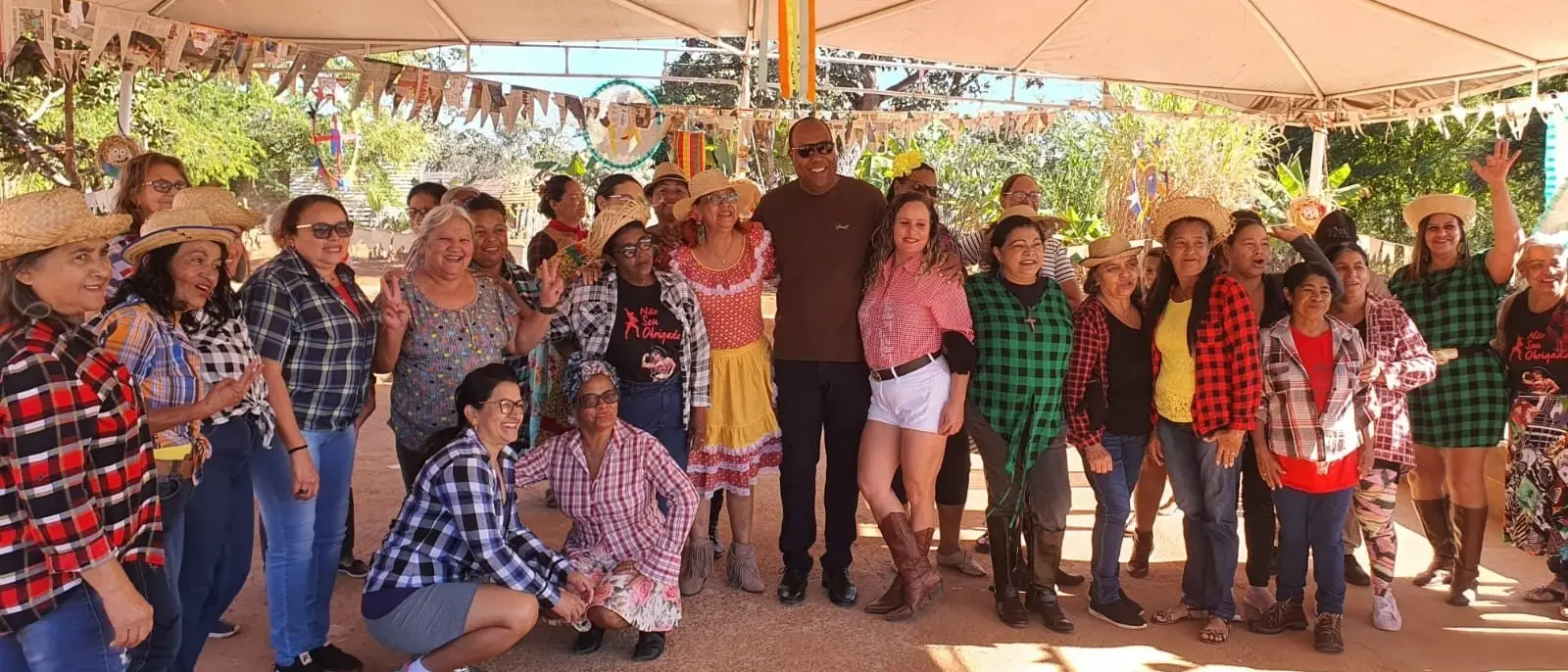 Grupo de idosos e convidados em trajes de festa junina posando sob uma tenda no Espaço Quilombo.