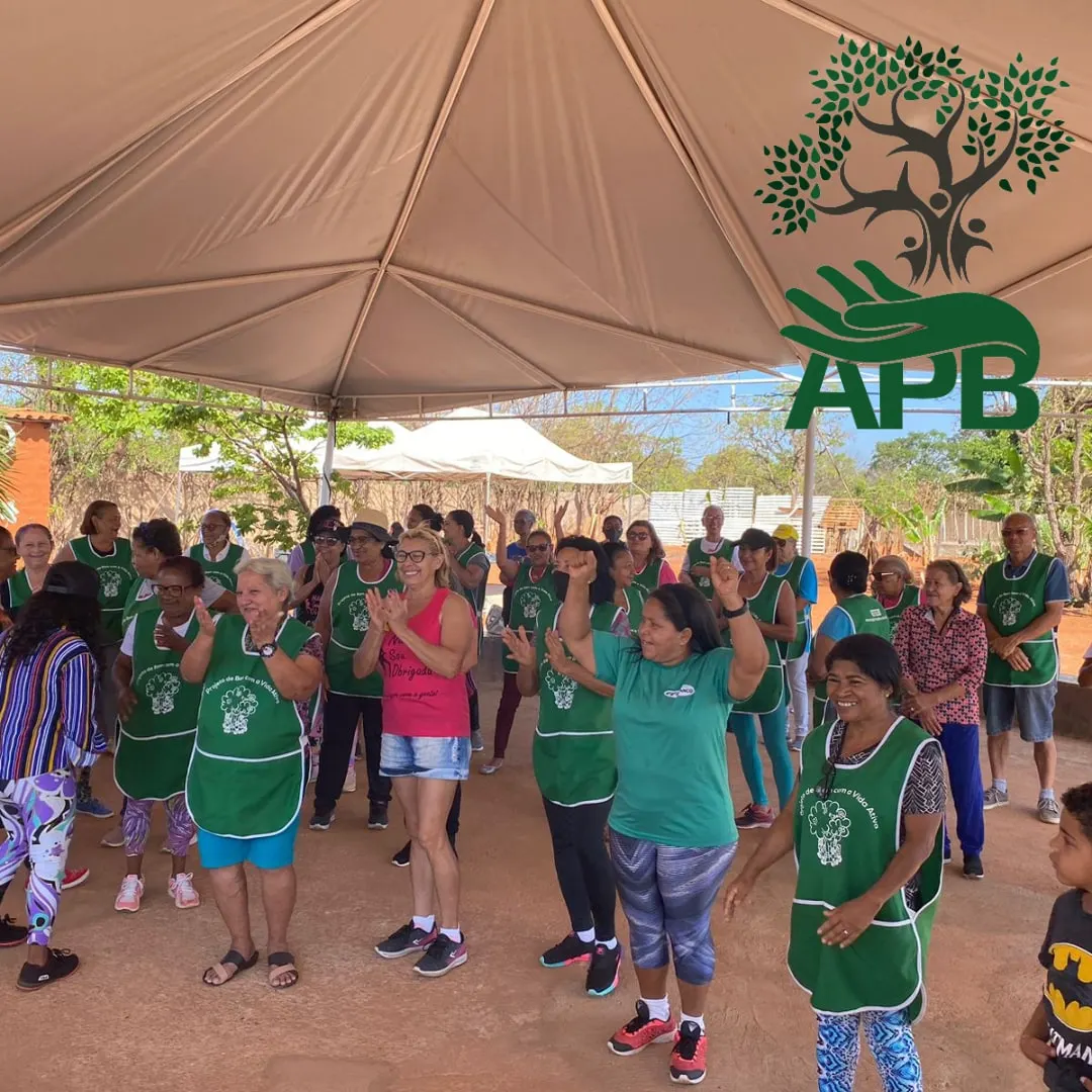 Mulheres de avental verde alongando-se em grupo sob uma tenda ao ar livre.
