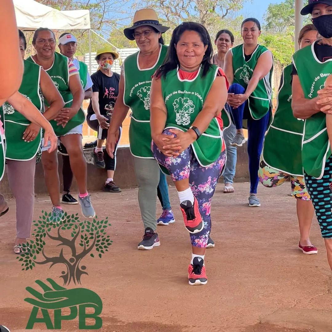 Mulheres de avental verde fazendo exercício em grupo ao ar livre.