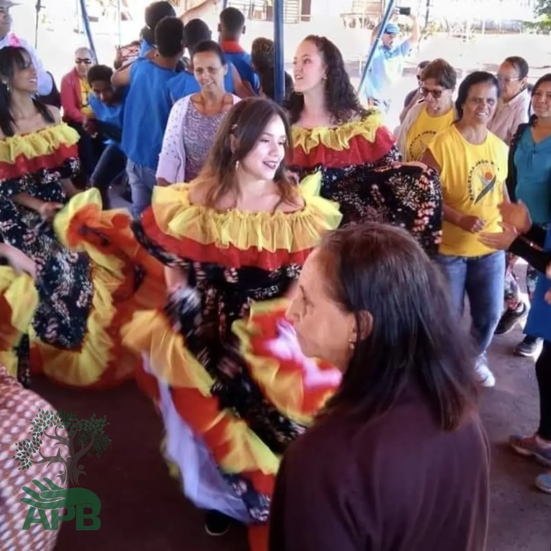Dançarinas em saias de quadrilha rodopiando em uma festa junina, com participantes ao fundo.