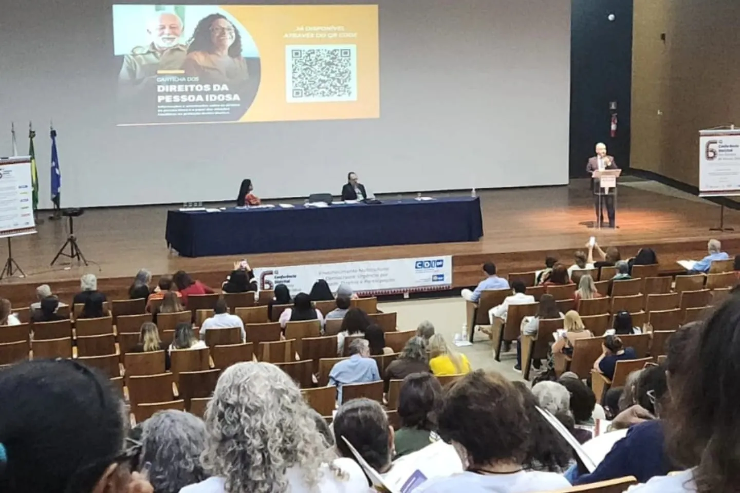 Auditório da 6ª Conferência Distrital dos Direitos da Pessoa Idosa, com o palco e o público sentado.