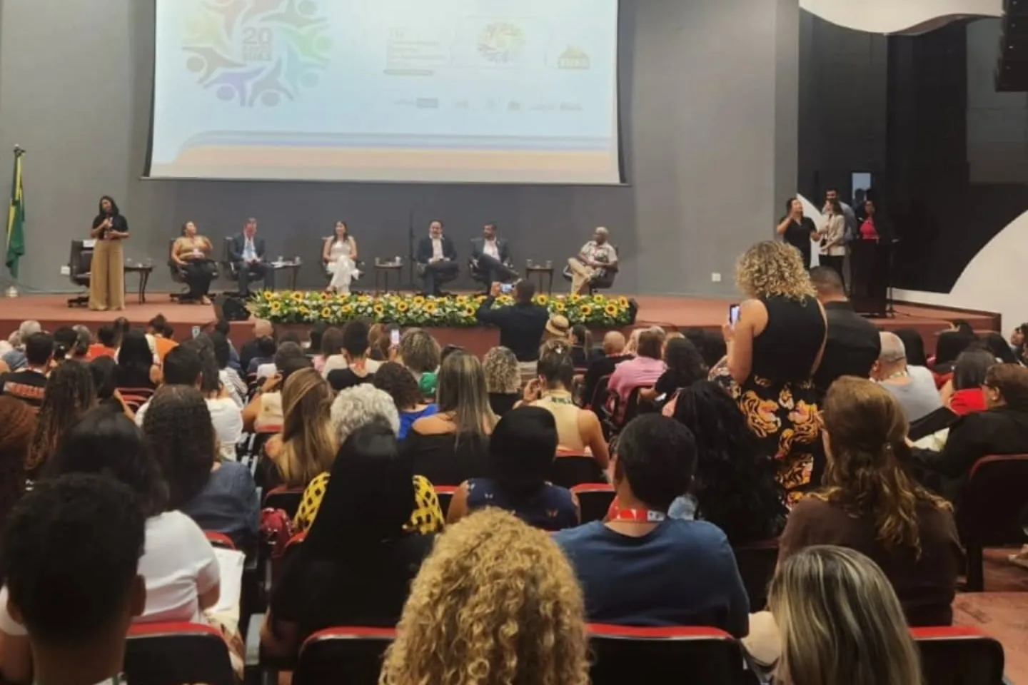 Auditório da Conferência de Assistência Social, com a mesa no palco e o público sentado.
