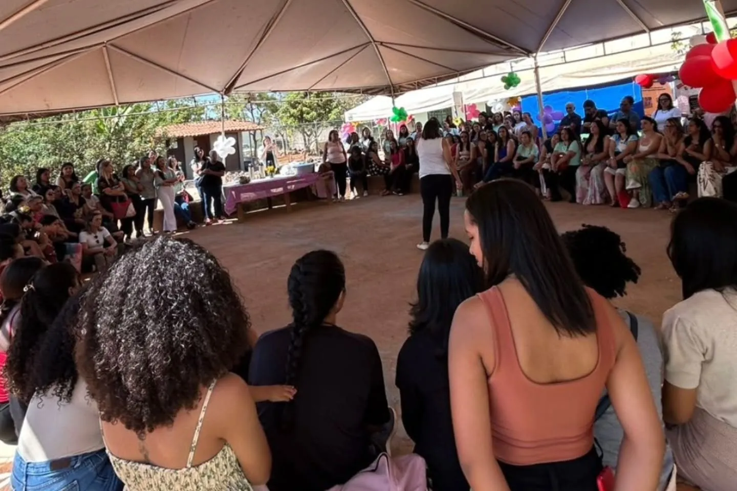 Formação pedagógica na sede da APB: colaboradoras das unidades sentadas em roda sob a tenda, de costas para a câmera.