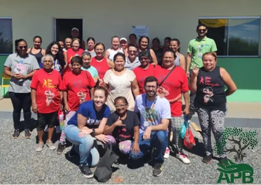 Grupo de adultos de camiseta vermelha posando, uns agachados e outros em pé, diante de um prédio verde.