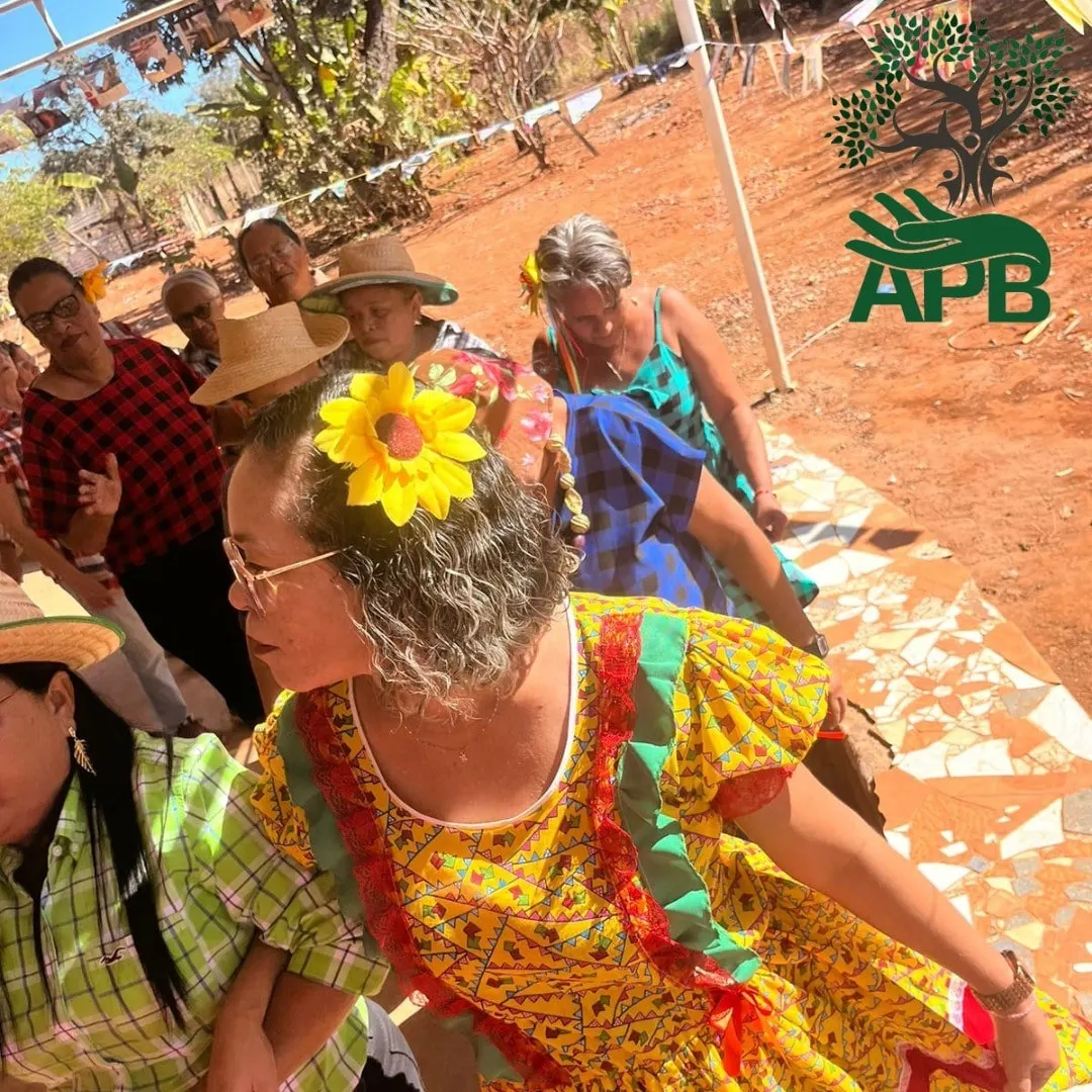 Mulher de vestido amarelo e flor no cabelo dança em uma festa junina ao ar livre.