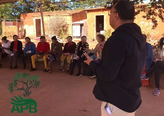 Palestrante de costas fala para idosos sentados em fila ao ar livre.