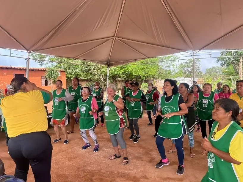 Idosas de avental verde dançando em grupo ao ar livre.