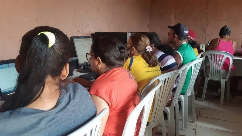 Pessoas em uma aula de informática diante de computadores, vistas de lado e de costas.